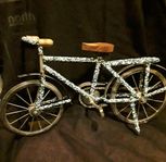Cykelmodell i metall präglad med vita pärlor i blå bakgru