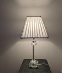 Bordslampa i glas med vit lamskärm.